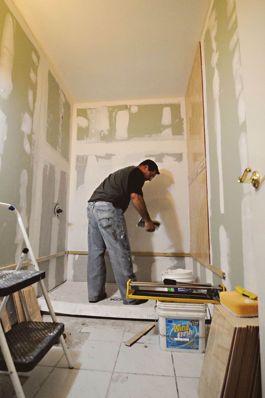 Tradesman spreading tile adhesive on a bathroom wall with a tile cutter nearby