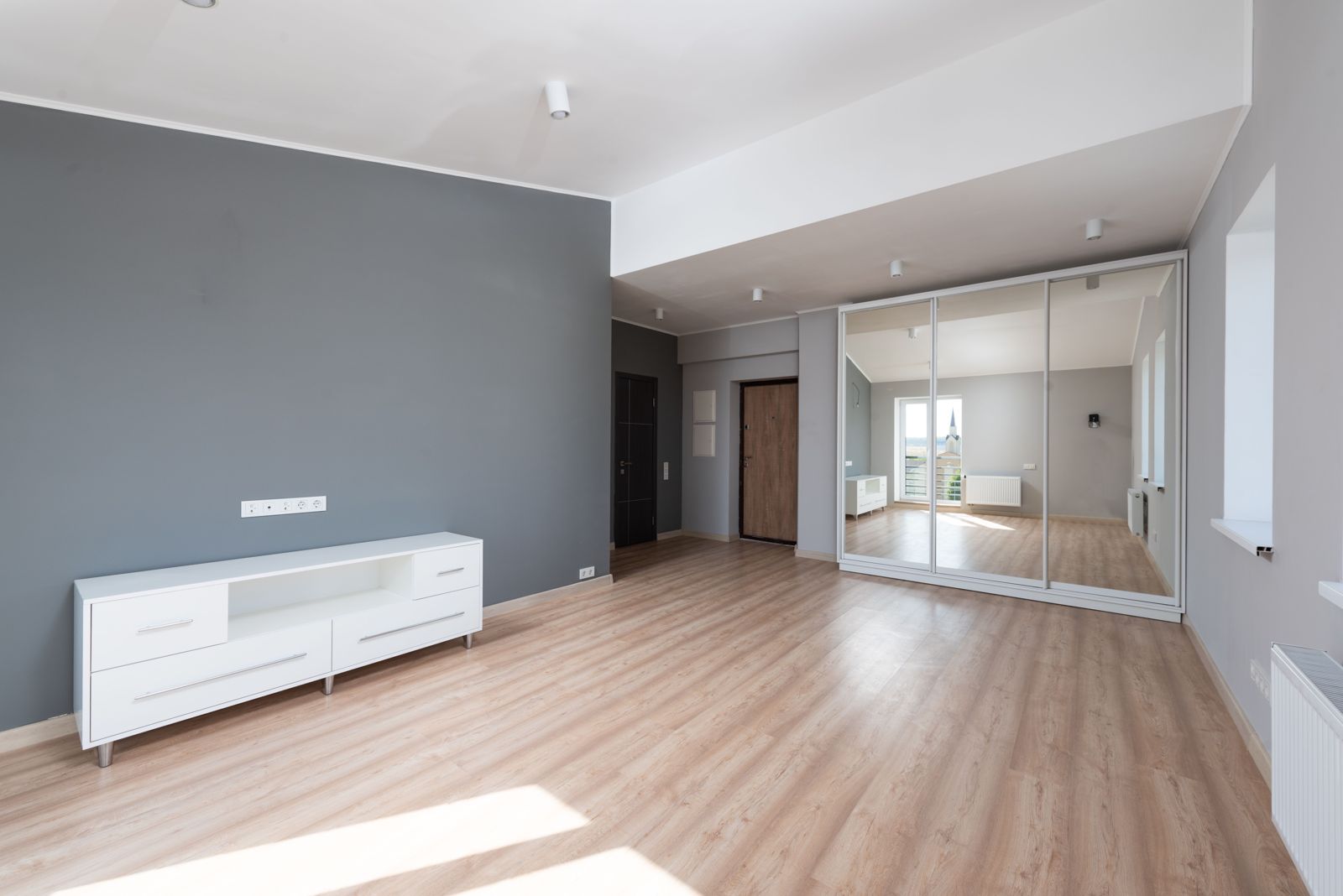 Sunlit room with a light wood-look plank floor running toward the hallway