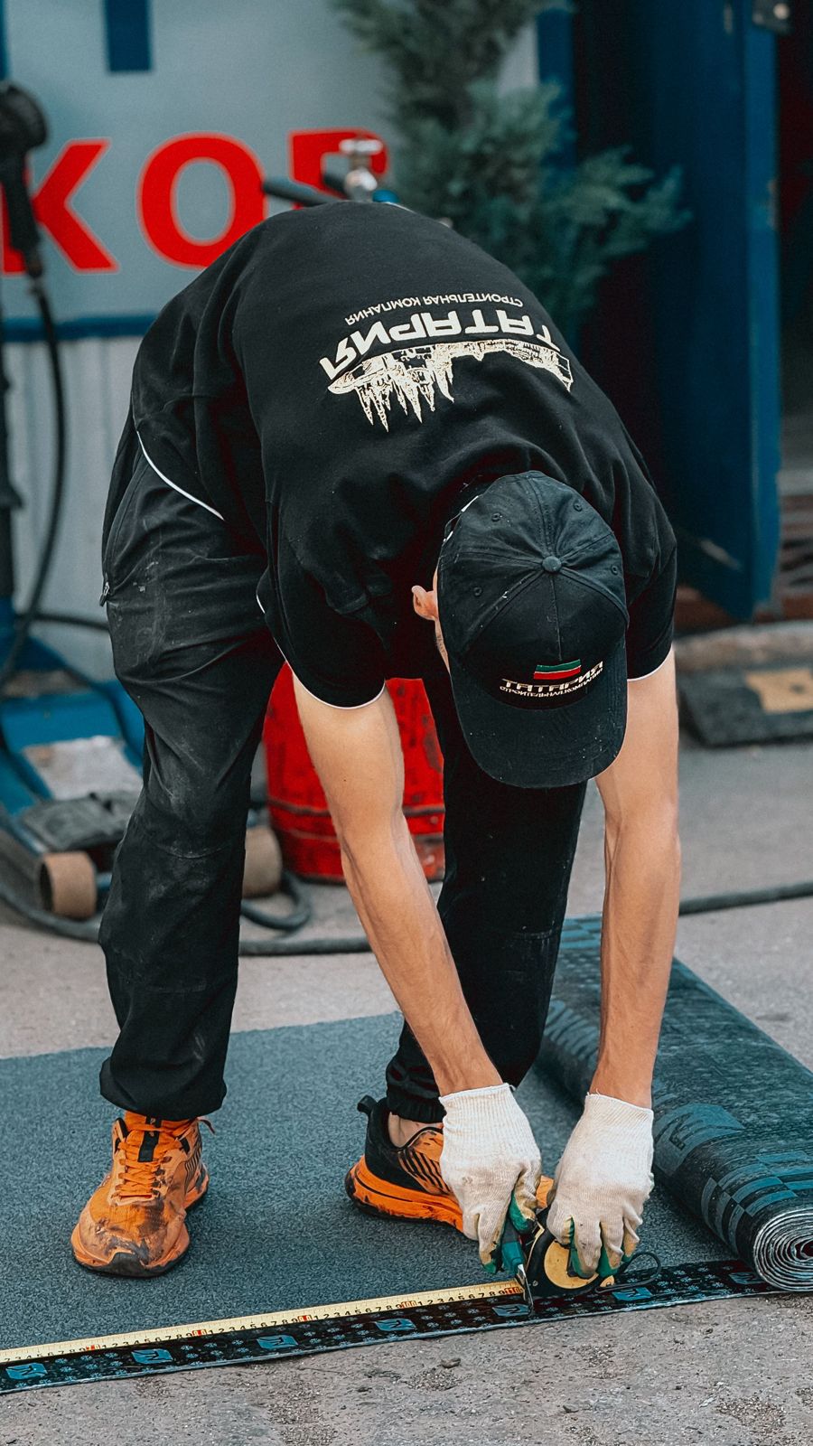Installer bending over to cut roll flooring material along a measuring tape