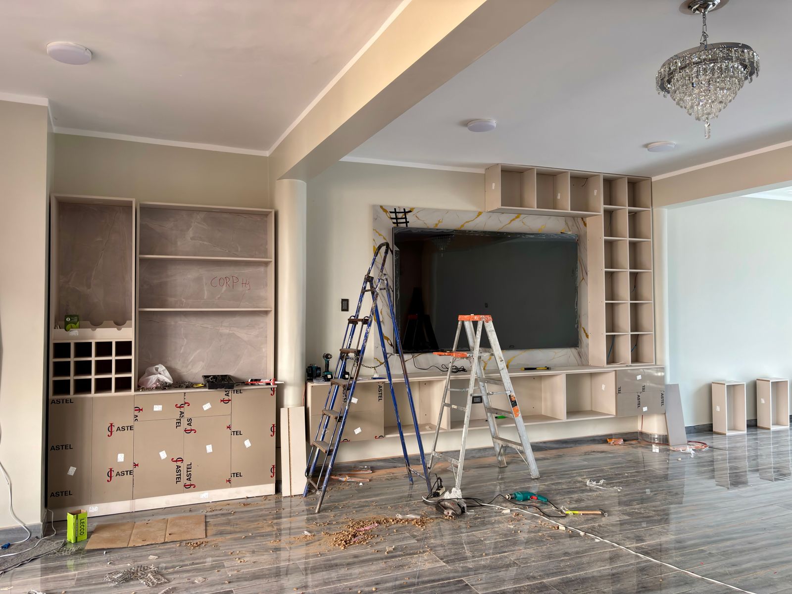 Large living room with a glossy grey tile floor, ladders and tools while cabinetry is installed